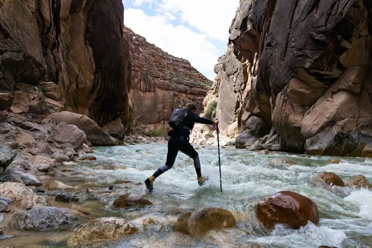Hiker using a trekking pole to cross a strong current in the Virgin River inside the Narrows canyon