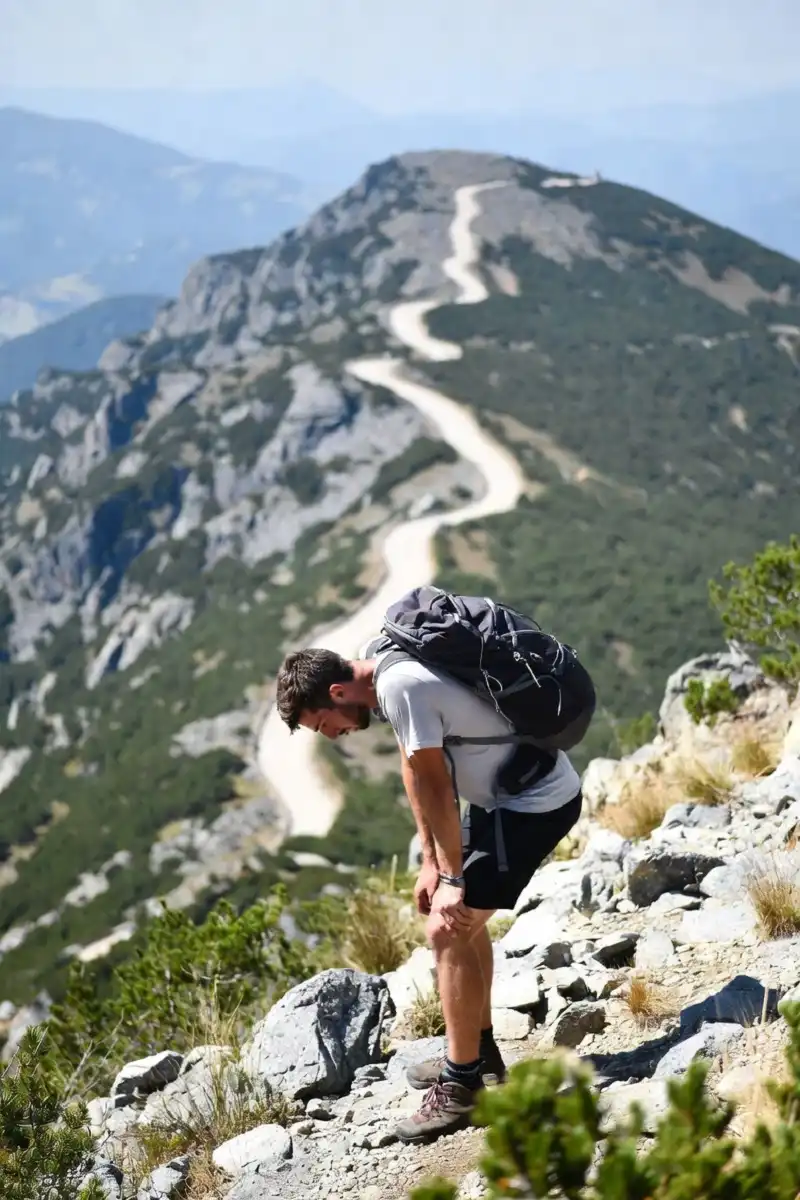 Tired hiker taking a break on a steep, rocky switchback trail during a strenuous climb