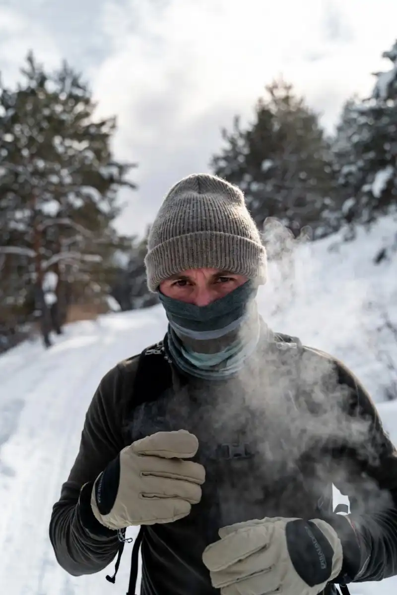 Hiker bundled in a wool beanie insulated gloves and neck gaiter on a snowy trail