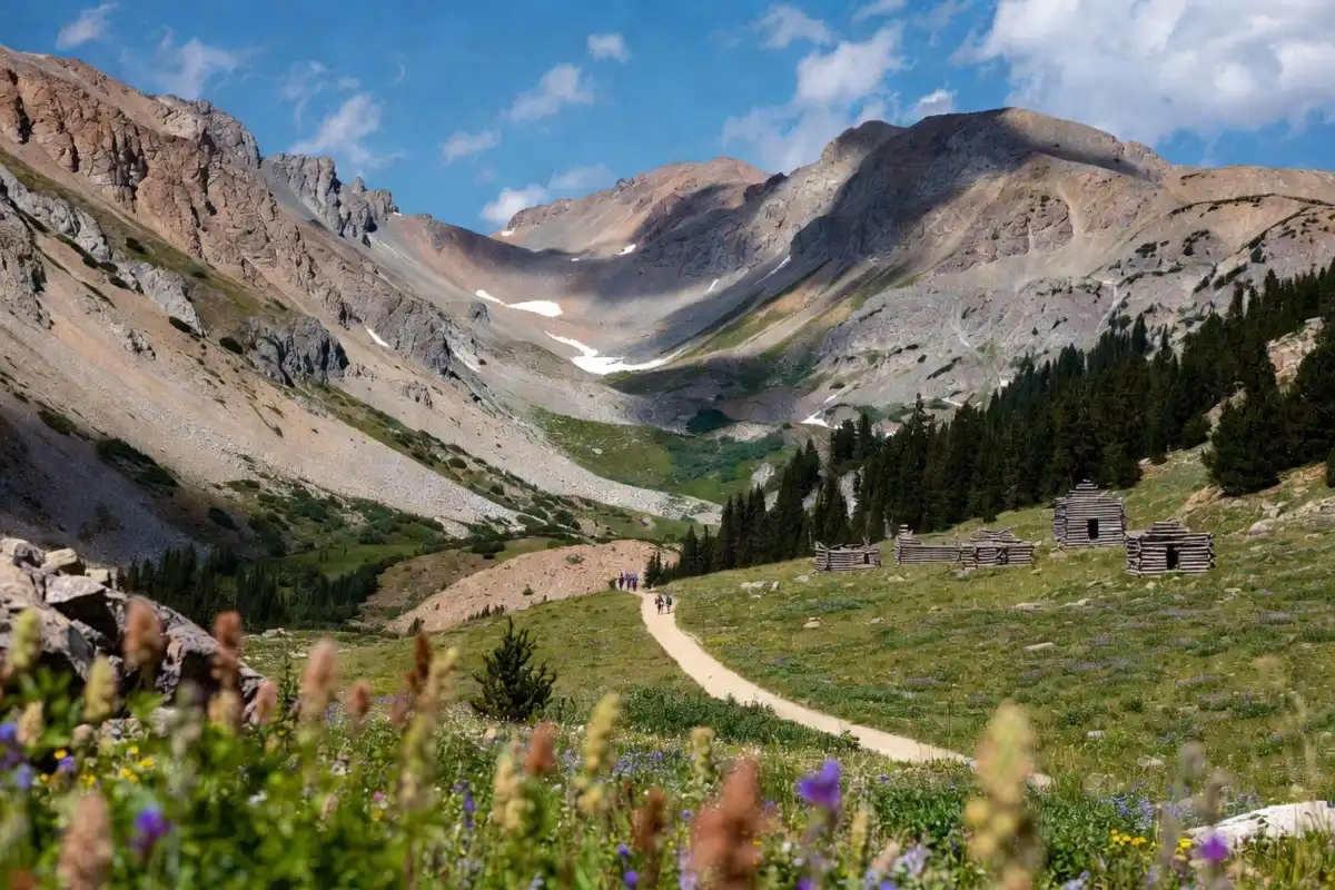 Hikers walking an old mining road toward weathered log cabin ruins in a wide alpine gulch near Copper Mountain Colorado