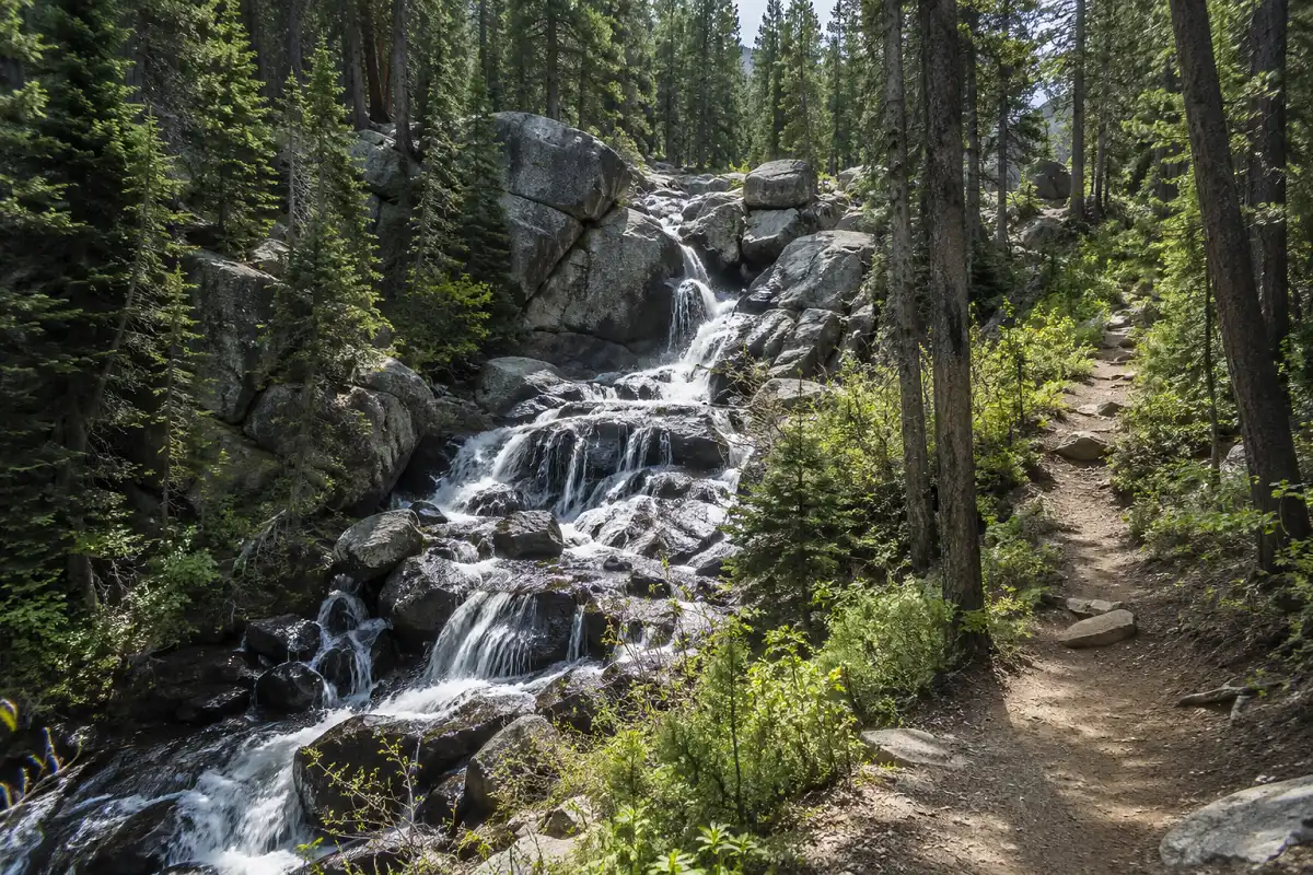 Small waterfall cascading over rocks along Jim Creek Trail in the forest near Winter Park, Colorado