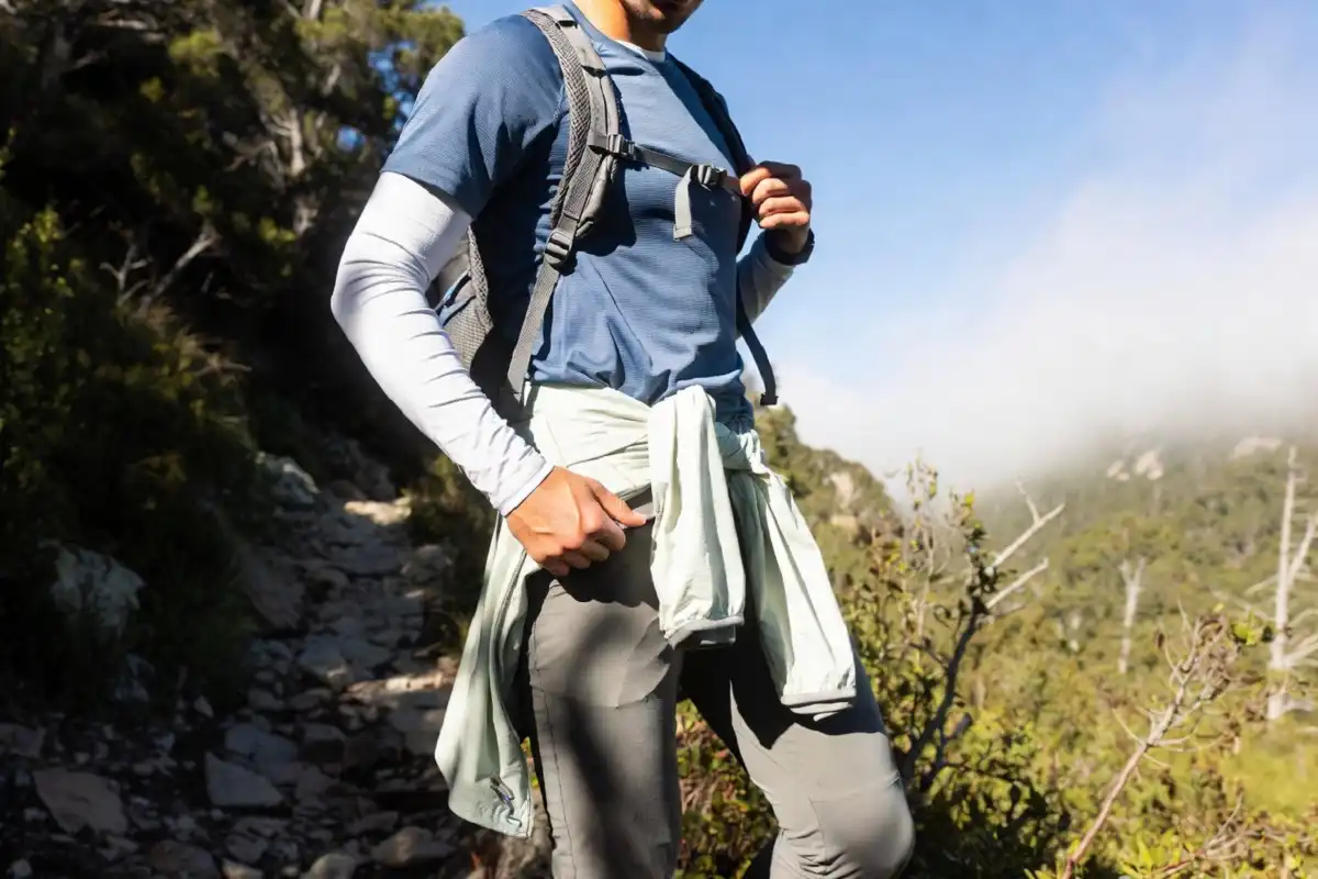 Hiker on a warm-weather trail carrying a lightweight layer tied around the waist as temperatures rise from a cool morning to a sunny afternoon.
