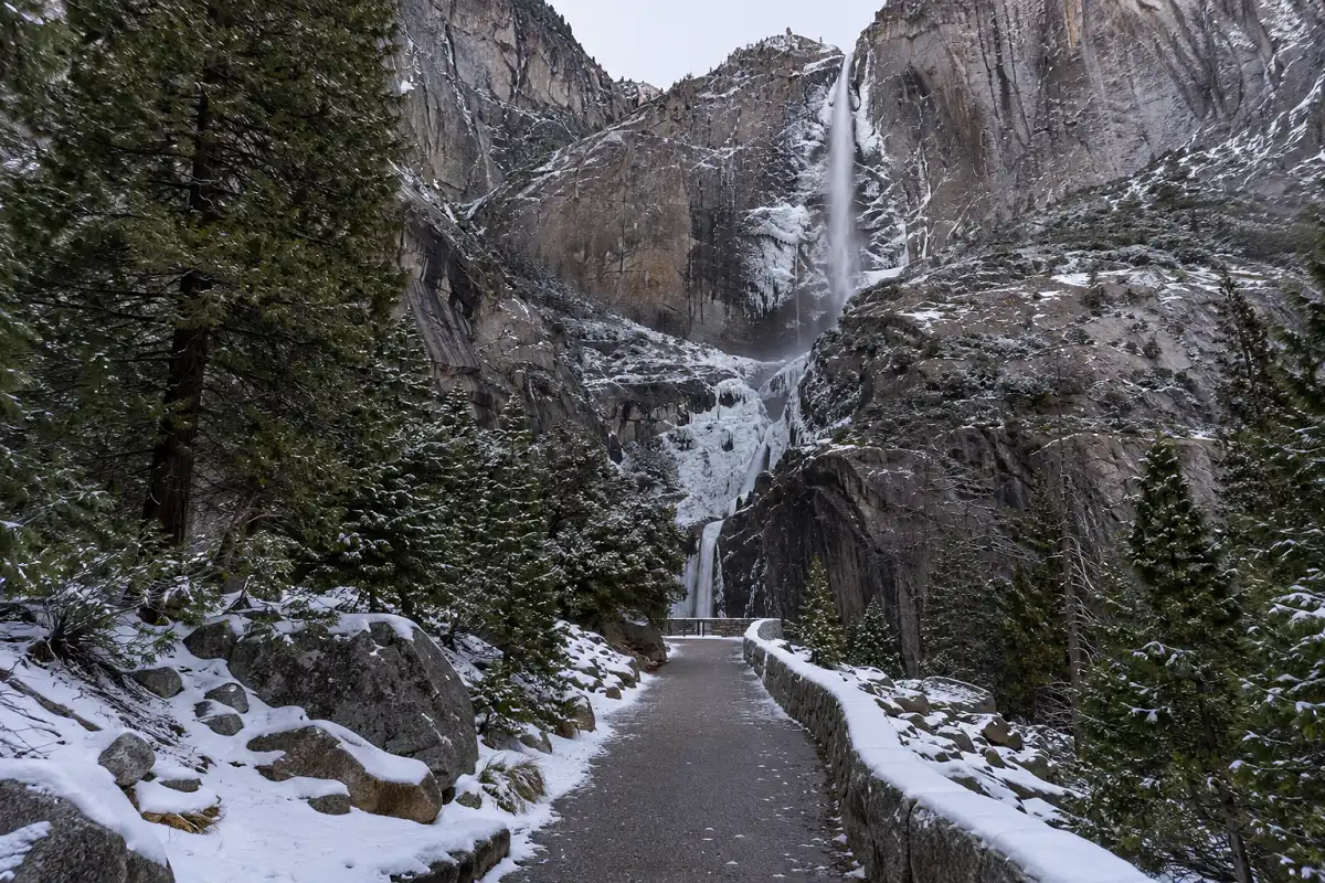 Lower Yosemite Fall Trail leading to Yosemite Falls with frozen winter spray on surrounding rocks.