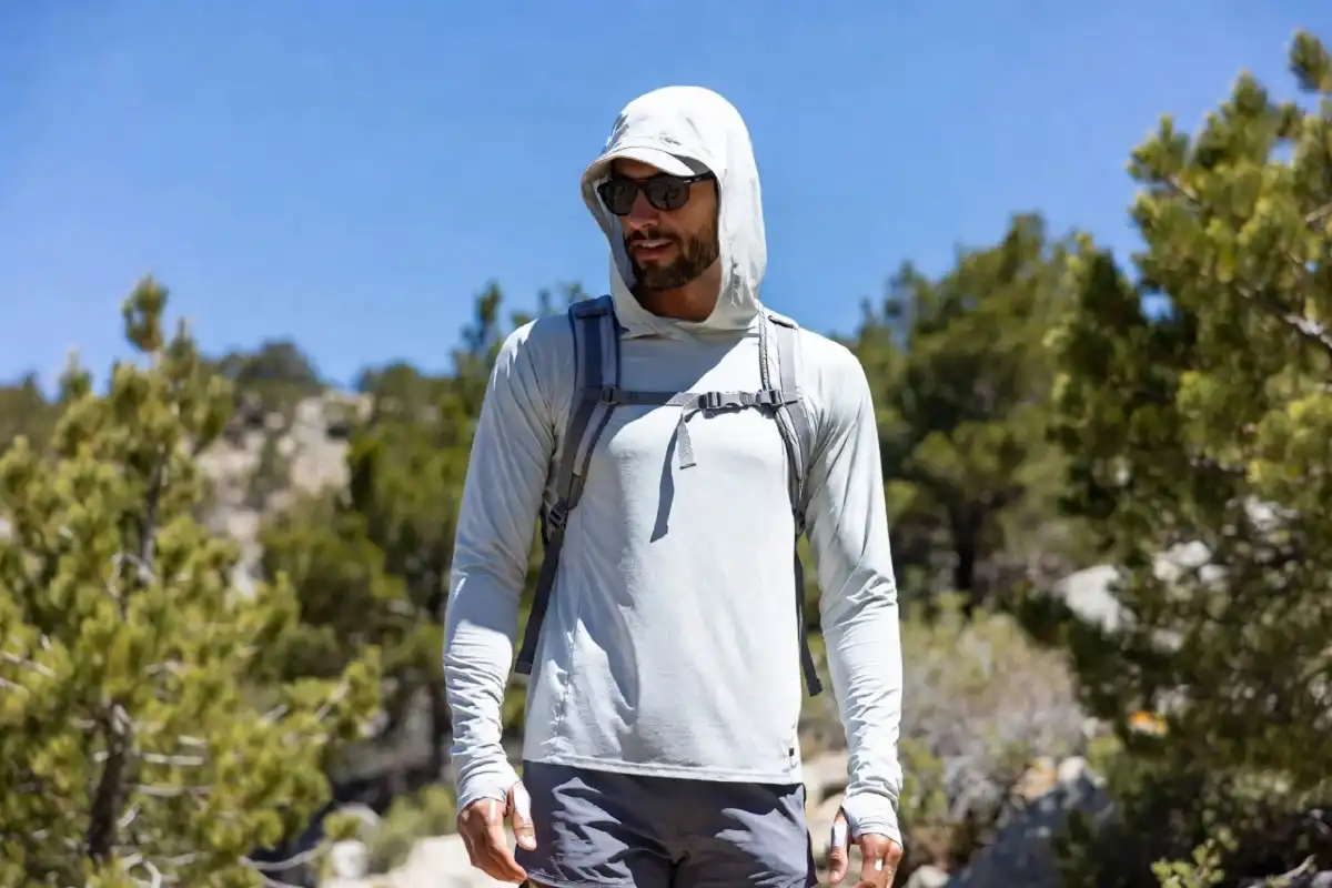 Hiker wearing a lightweight UPF-rated sun hoodie on a sunny mountain trail for breathable sun protection during a summer hike.