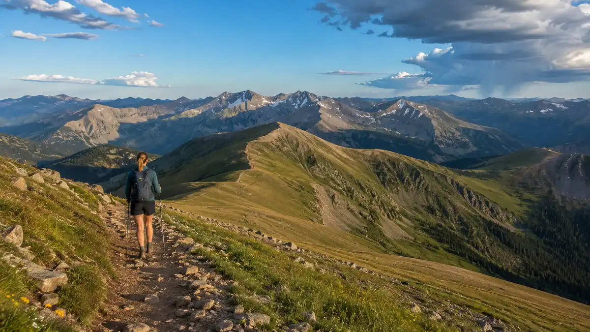 Solitary hiker on Vasquez Peak Trail above treeline near Winter Park, Colorado, surrounded by alpine meadows and rugged mountain peaks.