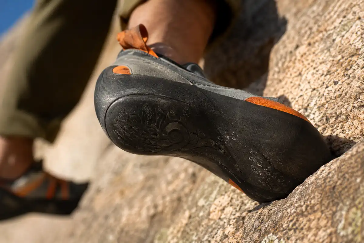 Sticky rubber sole of an approach shoe gripping granite rock during a climbing approach