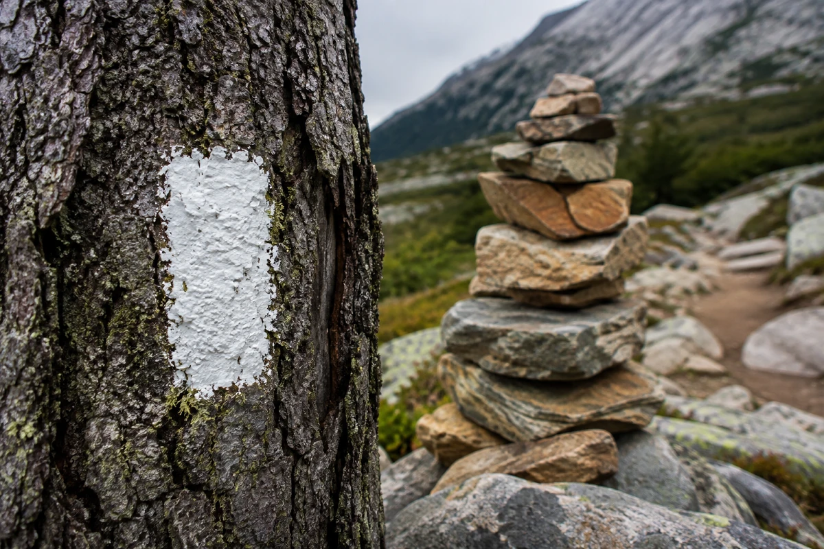 Painted trail blaze and stacked cairn used as trail markers for hiking navigation